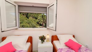Une chambre avec deux lits, une fenêtre donnant sur un paysage verdoyant, une table de chevet avec une lampe et une petite plante.