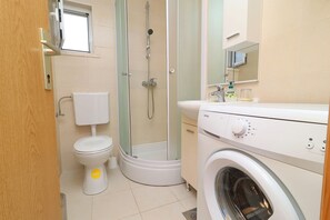 Ein kleines Badezimmer mit Toilette, Dusche und Waschmaschine.