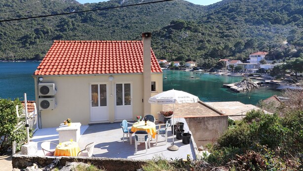 Un petit bâtiment avec un toit recouvert de tuiles rouges, une terrasse dotée de sièges extérieurs et une vue sur un lac et des montagnes.