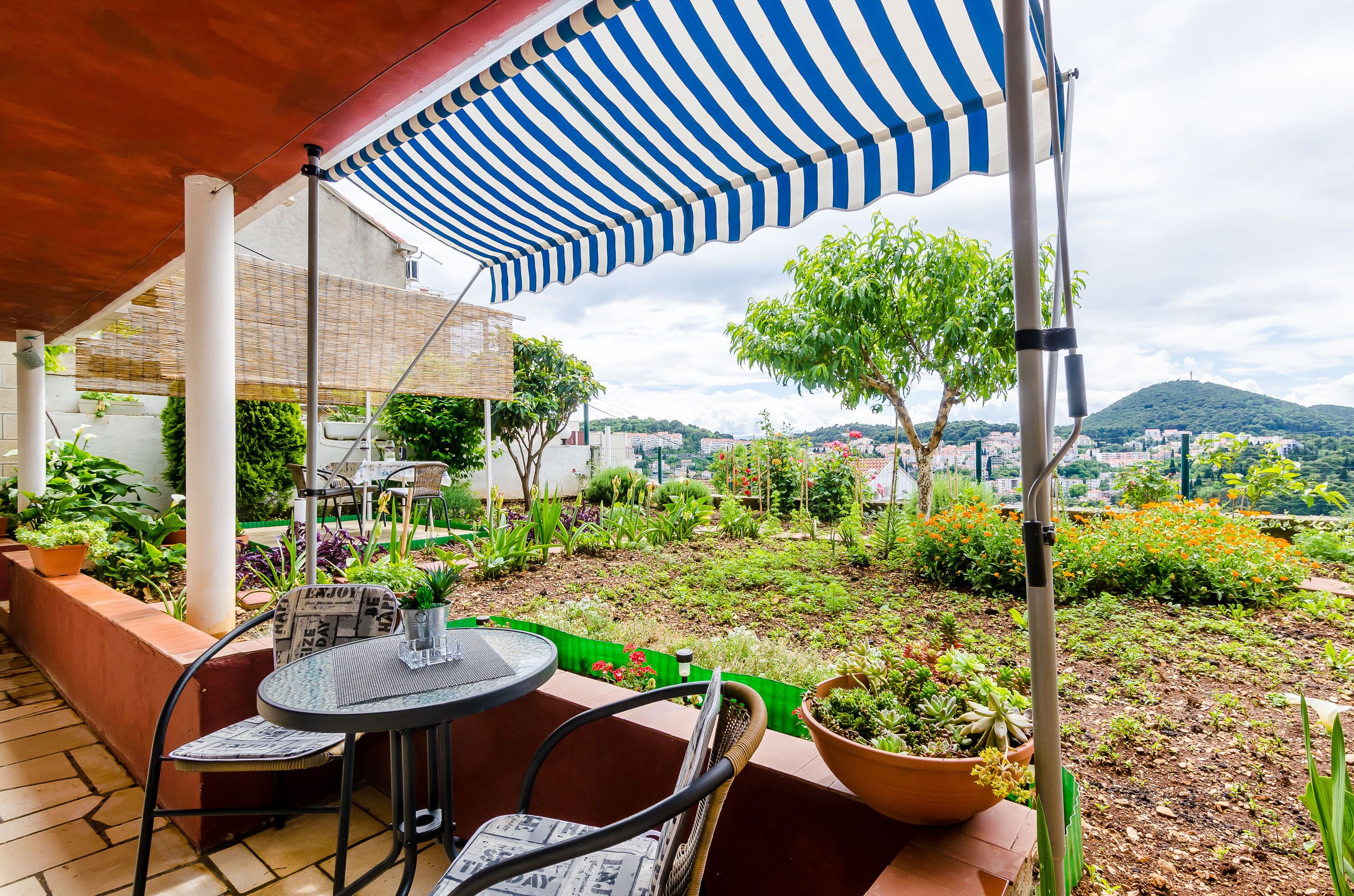 Un patio con un toldo a rayas, mobiliario exterior y vistas a un paisaje urbano y colinas.