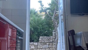 Ein offenes Durchgangsbild zu einer Steinmauer und Grünpflanzen, links ist eine Küche erkennbar.
