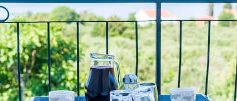 A table with a pitcher, cups, and sugar cubes on a balcony with a view of greenery and distant buildings.