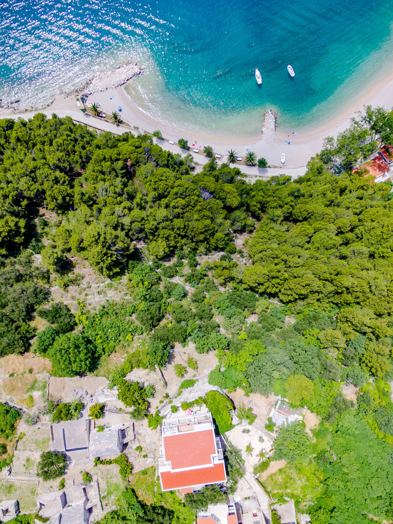 Eine Luftaufnahme einer Küstenregion mit Strand, Booten und einem Gebäude mit rotem Dach.