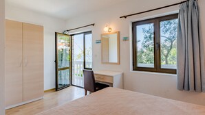 A bedroom with a bed, a desk, a chair, a wardrobe, and a large window with curtains. - Villa Kosa - Standard Double Room With Balcony and Sea View (Soba 1-Matija) (Brela)