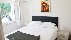 Une chambre à coucher avec un lit, une table de chevet, une lampe, un tableau et une fenêtre donnant sur un oiseau bleu.