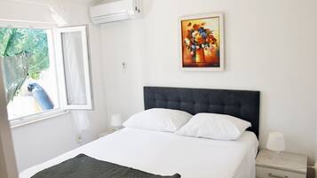 Un dormitorio con cama, mesita de noche, lámpara, cuadro y ventana con vista a un pájaro azul.