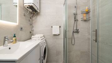 Un bagno moderno con lavandino, lavatrice e box doccia in vetro.