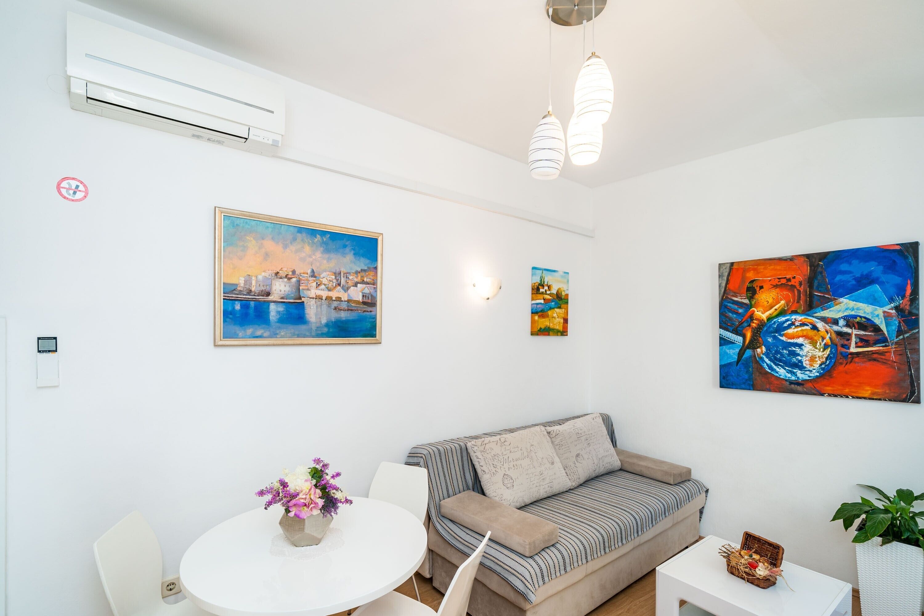 A modern living room with a sofa, a dining table with chairs, and artwork on the walls.