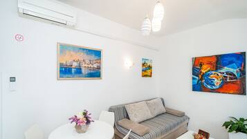 A modern living room with a sofa, a dining table with chairs, and artwork on the walls.