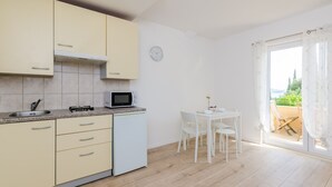 A modern kitchen with a microwave, sink, and cabinets. There is a dining area with a table and chairs. A clock is on the wall. - Color Apartments - Comfort One Bedroom Apartment with Terrace and Partial Sea View (Mlini)