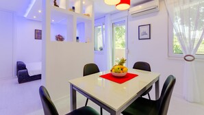 A modern dining area with a table, chairs, and a fruit bowl. There are shelves with decorative items and a window with curtains. - Studio Luce Mala (ST) - Studio with Terrace (Split)