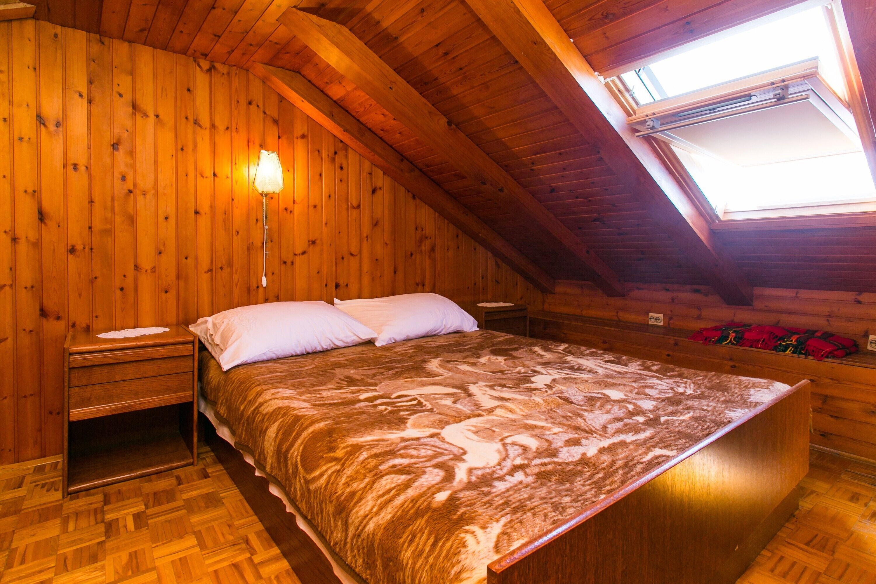 Une chambre confortable située sous les toits, avec un grand lit, des murs en bois, une lucarne et une table de chevet avec une lampe.