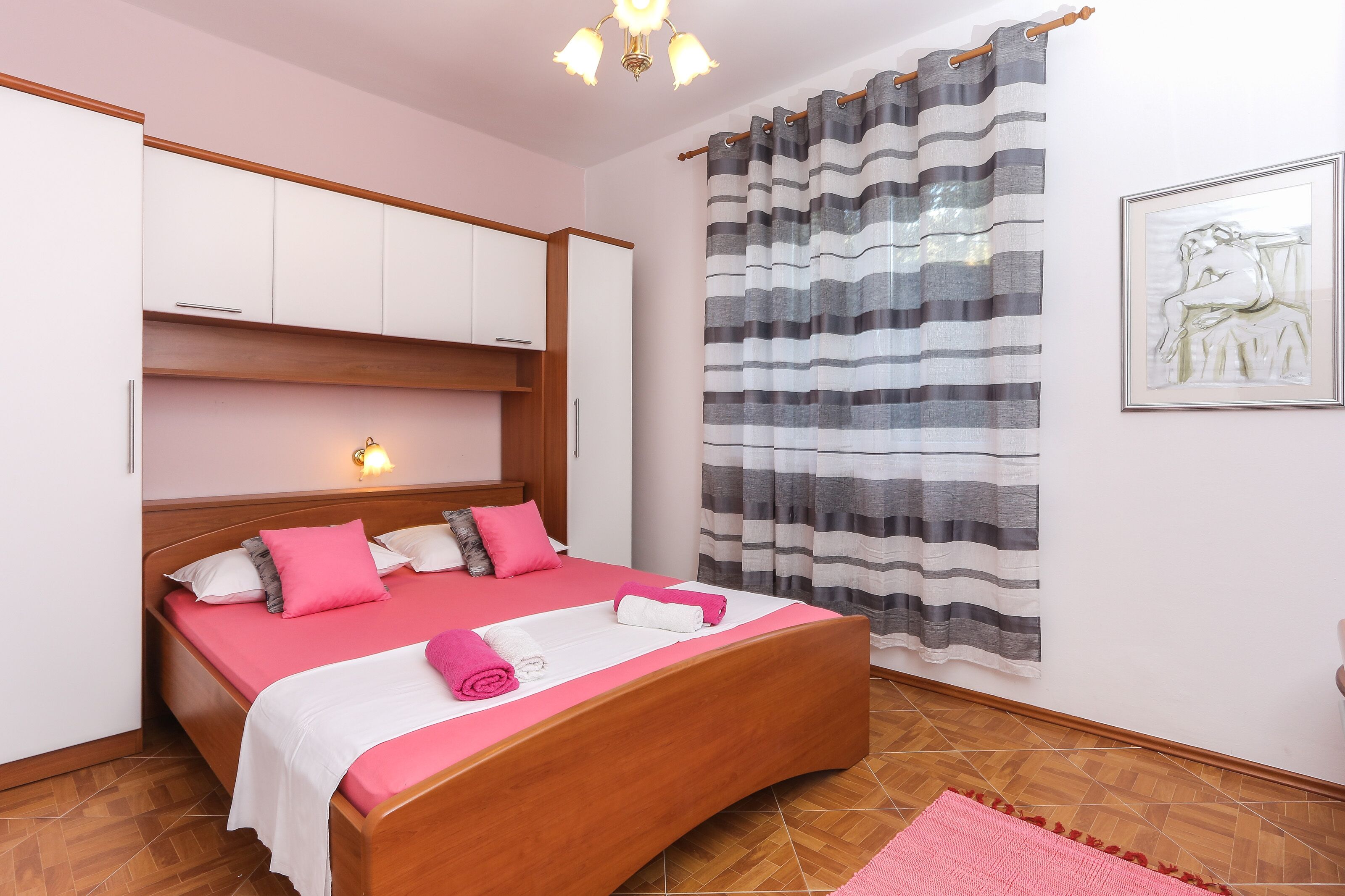 A bedroom with a wooden bed, a headboard with built-in lighting, a striped curtain, and a framed artwork on the wall.