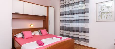 A bedroom with a wooden bed, a headboard with built-in lighting, a striped curtain, and a framed artwork on the wall.