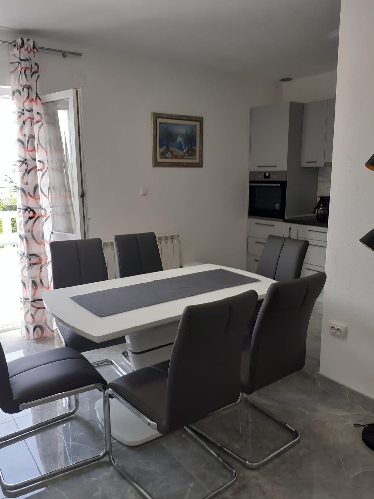 A modern dining area with a rectangular table, six chairs, and a view of the kitchen in the background.