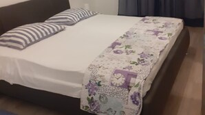 A neatly made bed with a floral bedspread and striped pillows, a dark headboard, and a painting on the wall.