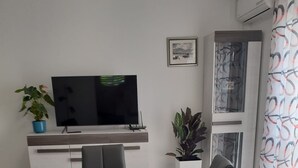 A modern office space with a long table, black chairs, a flat-screen TV, potted plants, and a patterned curtain.