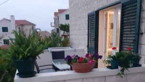 A balcony with a laptop, potted plants, and a window with green shutters.