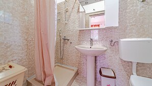 Een badkamer met douche, wastafel, toilet en een prullenbak.