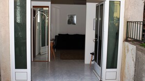 An open sliding glass door leading into a room with a dark-colored sofa, a small table, and a framed picture on the wall. - Apartment Basic - One Bedroom Apartment (Dubrovnik)