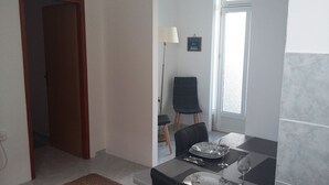 A dining area with a table set for two, a chair, a floor lamp, and a door leading to another room. - Apartment Basic - One Bedroom Apartment (Dubrovnik)