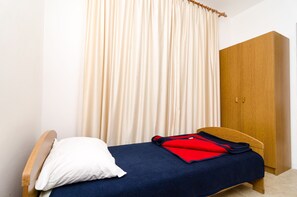 Un letto singolo con cuscino bianco e coperta blu, un armadio in legno e una tenda color beige.