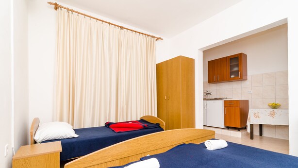A room with two beds, a wooden wardrobe, a small kitchen area with a table and cabinets, and a curtain. - Guest House Kiko - Studio (A3) (Pomena)
