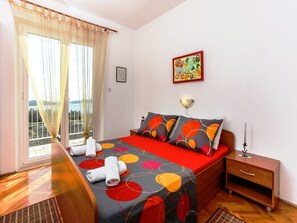 Un dormitorio con cama, mesita de noche, lámpara de pared y ventana con cortinas.