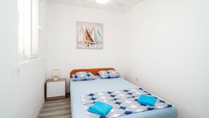 Una habitación pequeña y luminosa con una cama, una mesita de noche y un ventilador de techo.