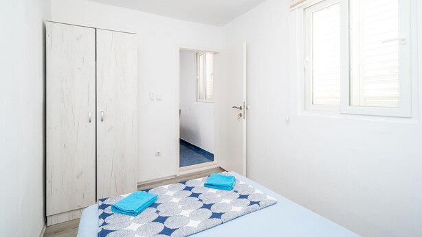 Un dormitorio con cama, armario, ventana y puerta que da a un pasillo.