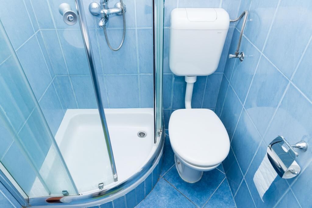 Un bagno con doccia vetrata, un WC bianco e pareti rivestite di piastrelle blu.