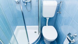 Une salle de bain avec une douche à parois de verre, des toilettes blanches et des murs recouverts de carreaux bleus.