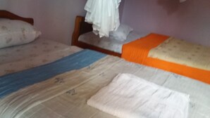 A room with two beds, one with a blue blanket and the other with an orange blanket. There is a wooden headboard and a white curtain on one bed.