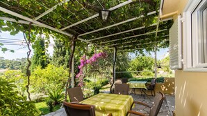 A covered patio with a table and chairs, surrounded by greenery and a view of the landscape. - Guest House Kanjuo - Studio Apartment with Terrace and Garden View (Mlini)