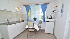 A modern kitchen with white cabinets, a central island, and a dining area with chairs and a table. - Guest House Kanjuo - Studio Apartment with Terrace and Garden View (Mlini)