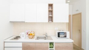 Una cocina moderna con armarios blancos, un fregadero, una tetera, un microondas y una cesta de frutas.
