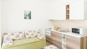 Una kitchenette pequeña con microondas, pileta y placares. Hay un sofá verde con almohadones estampados y un cuadro en la pared.