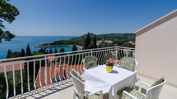Balcón con mesa y sillas con vista al mar, una piscina y edificios.