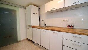 Una cocina con armarios blancos, encimera de madera, pileta de acero inoxidable y refrigerador.