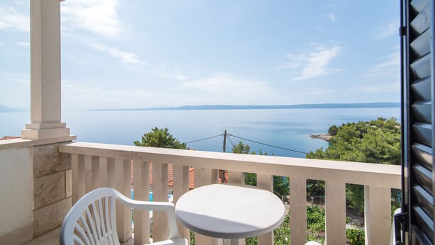 A balcony with a white chair and table, overlooking a body of water and greenery. - Apartments Neva- Two Bedroom Apartment with Balcony (4R) (Selca)