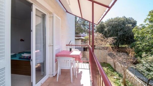 A balcony with a table and chairs, a sliding glass door, and a view of the surrounding garden.