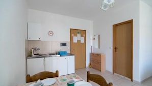 A compact kitchen with white cabinets, a microwave, and a sink. There is a dining table with chairs and a small refrigerator.