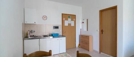 Eine kompakte Küche mit weißen Schränken, einer Mikrowelle und einem Spülbecken. Es gibt einen Esstisch mit Stühlen und einen kleinen Kühlschrank.