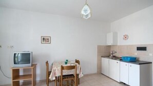 A compact kitchen with a dining table, chairs, a television on a stand, and cabinets.