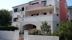Ein zweistöckiges Gebäude mit Balkon, kleinem Rundbogenportal und Topfpflanzen.