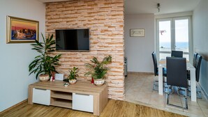 A modern living room with a stone wall, a flat-screen TV, a wooden coffee table, and potted plants. - Sea View Apartments - Two Bedroom Apartment with Balcony and Sea View Lenka (Dubrovnik)