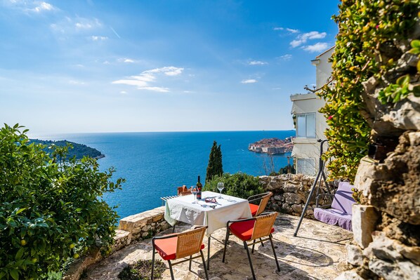 A table set with a white tablecloth, red cushions, and a bottle of wine, overlooking a coastal view.