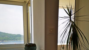 A room with a view of a body of water, a large potted plant, a woven mat on the floor, and a small table with a bowl on it. - Apartment with Balcony and  Sea View(Merivo) (Dubrovnik)