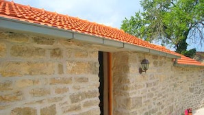 A stone building with a tiled roof, a doorway, and potted plants on the ground. - Stone House Harmony - One Bedroom Apartment with Patio and Garden View ( 1 ) (Zrnovo)