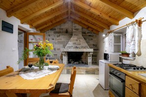 Una cocina acogedora con chimenea de piedra, techo de madera y una mesa de comedor adornada con flores y copas de vino.